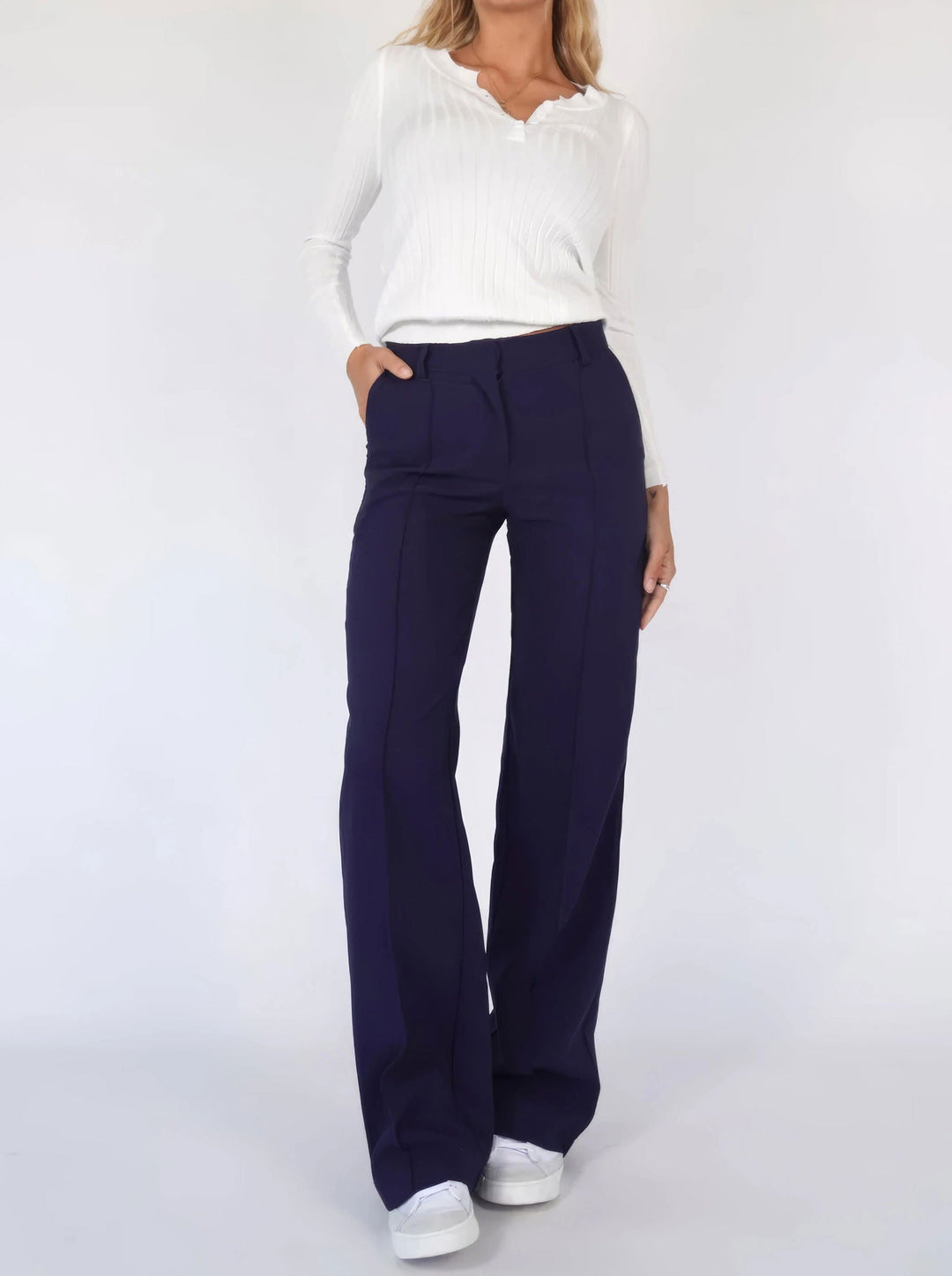 Donna con pantaloni a zampa blu scuro e maglia bianca a maniche lunghe, scarpe da ginnastica bianche. Moda casual elegante, abbigliamento femminile.