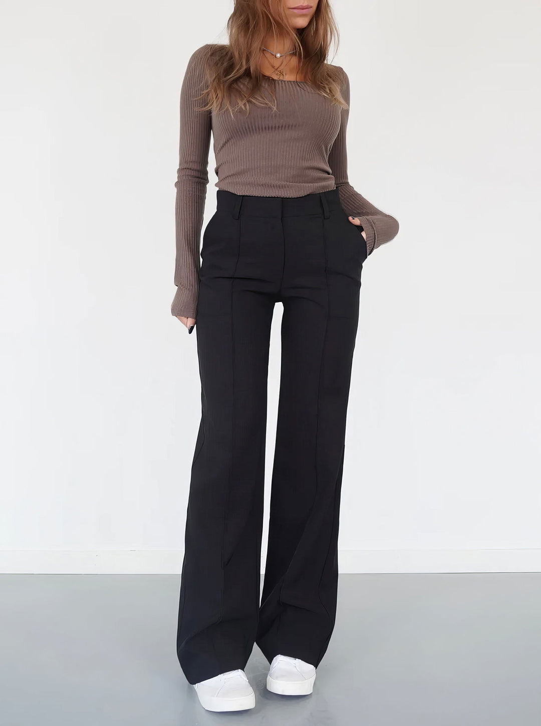 Donna in maglia marrone e pantaloni neri a zampa, scarpe bianche. Moda casual autunnale, abbigliamento femminile elegante e confortevole.