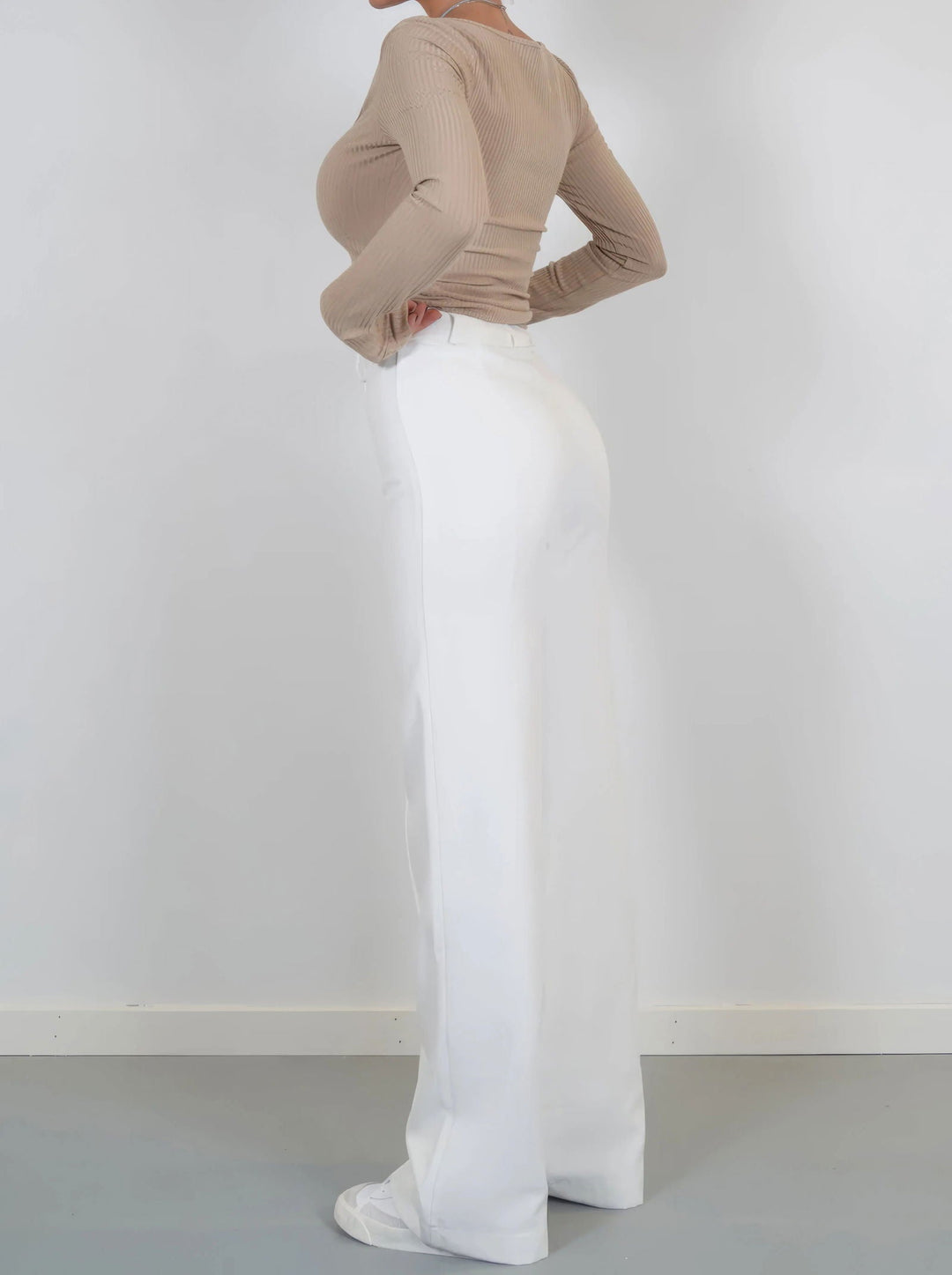 Pantaloni bianchi a vita alta da donna, taglio ampio, abbinati a maglia beige a maniche lunghe. Stile elegante e moderno, perfetto per ogni occasione.