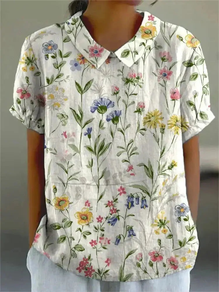 Camicia donna a maniche corte con stampa floreale colorata, colletto classico, sfondo bianco. Moda estiva casual, tessuto leggero.