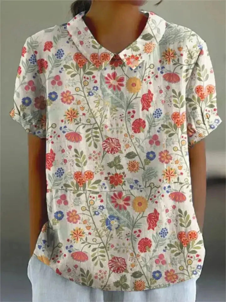 Camicia donna a maniche corte con stampa floreale colorata, colletto classico, sfondo bianco. Moda estiva casual, tessuto leggero.