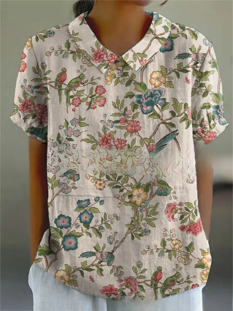 Camicia donna a maniche corte con stampa floreale e uccelli, colletto classico, sfondo bianco, stile casual estivo, tessuto leggero e traspirante.