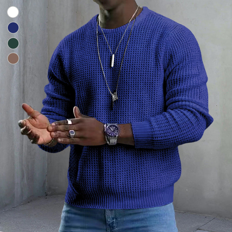 Maglione uomo blu a maglia grossa, indossato con jeans. Accessori: collane, orologio, anelli. Moda casual autunnale, stile urbano elegante.