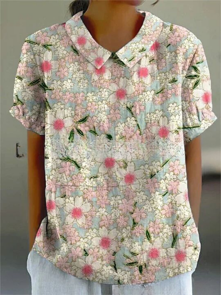 Camicia donna a maniche corte con colletto, fantasia floreale rosa e bianca su sfondo azzurro, stile casual estivo.