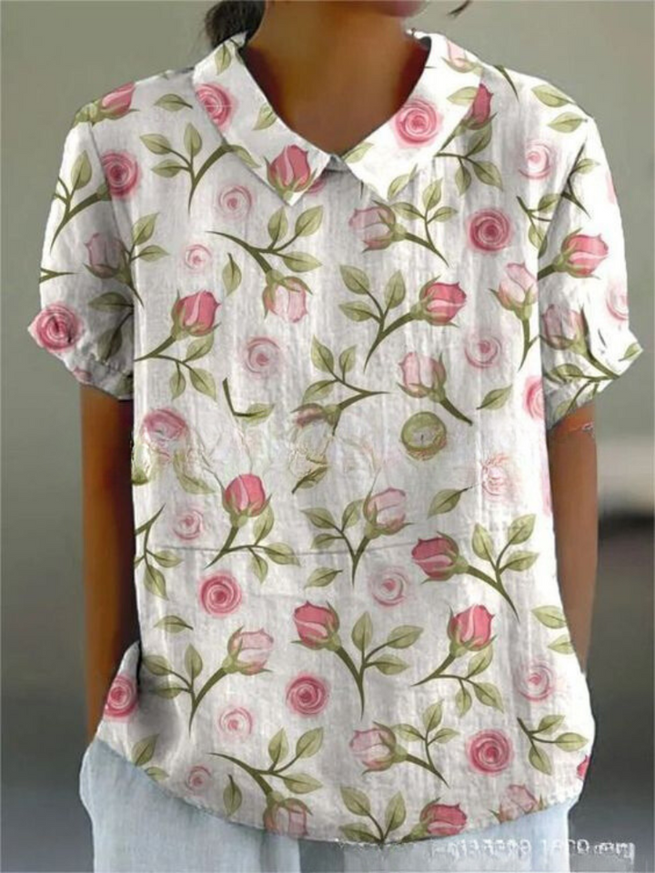 Camicia donna a maniche corte con stampa floreale rosa su sfondo bianco, colletto classico. Moda estiva casual, tessuto leggero e traspirante.