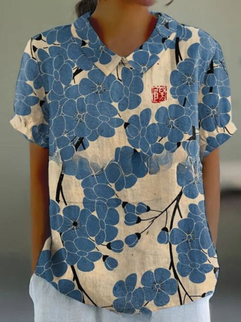 Camicia donna floreale blu, maniche corte, colletto classico, motivo fiori su sfondo beige. Stile casual, tessuto leggero, ideale per l'estate.