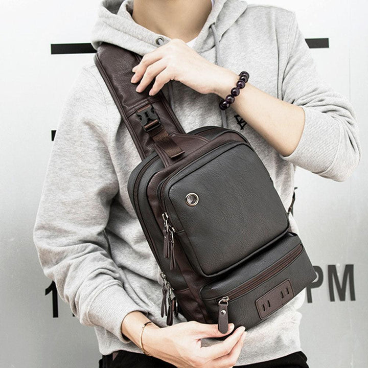 Zaino a tracolla in pelle marrone scuro, indossato da uomo con felpa grigia. Design moderno, ideale per viaggi e uso quotidiano.