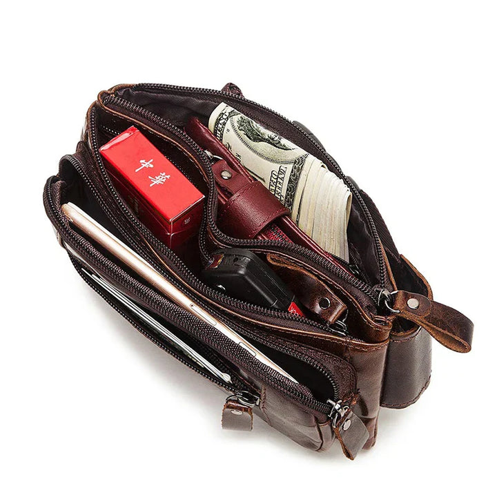 Borsa a tracolla in pelle marrone con scomparti aperti, contenente banconote, sigarette, smartphone e portafoglio. Accessorio moda uomo elegante.