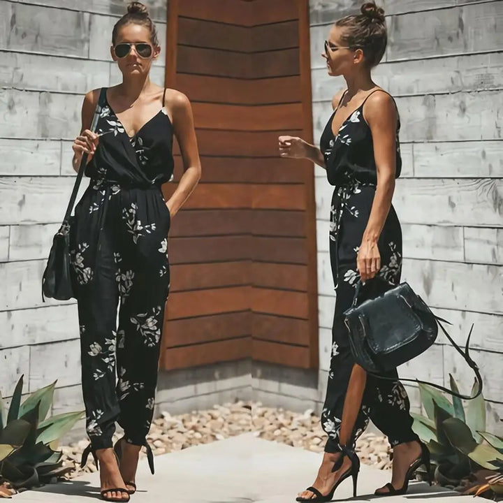 Donna con tuta nera floreale, sandali con tacco e borsa a tracolla. Moda estiva elegante, look casual chic. Sfondo in legno e piante.