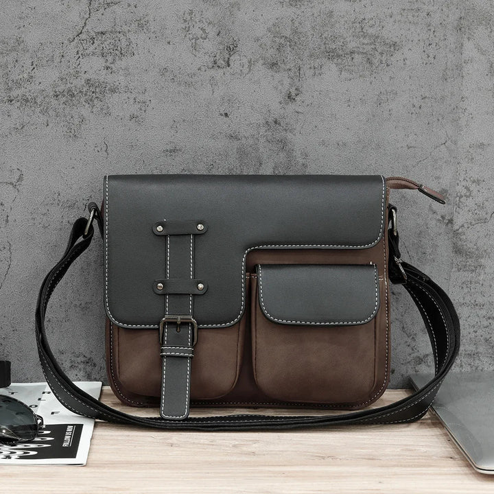 Borsa a tracolla in pelle marrone e nera su sfondo grigio, design elegante con tasche frontali, ideale per uomo, accessorio moda casual.