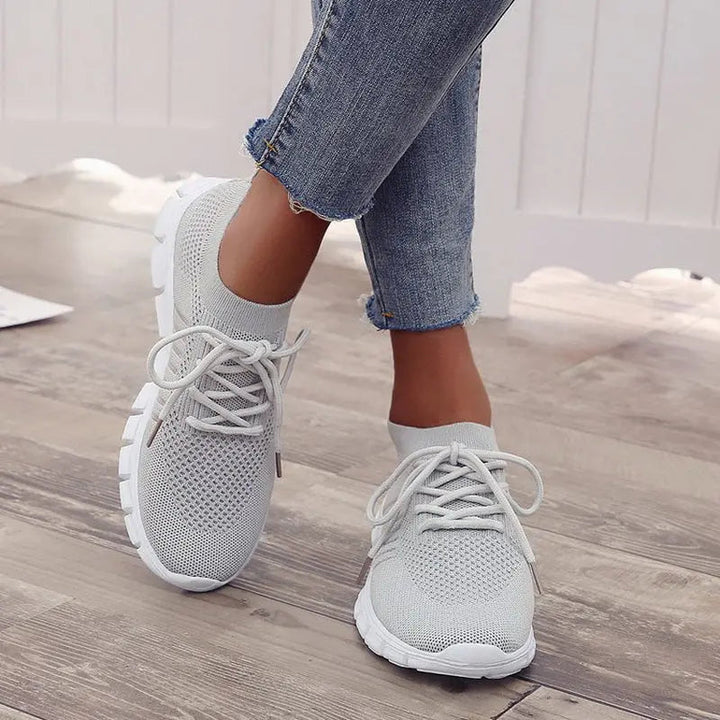 Scarpe da ginnastica bianche da donna, design traspirante in maglia, suola antiscivolo, indossate con jeans. Ideali per sport e tempo libero.