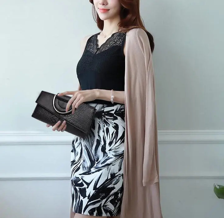 Donna elegante con abito nero e bianco a fantasia, cardigan beige, borsa nera con manico metallico. Moda femminile, abbigliamento chic.