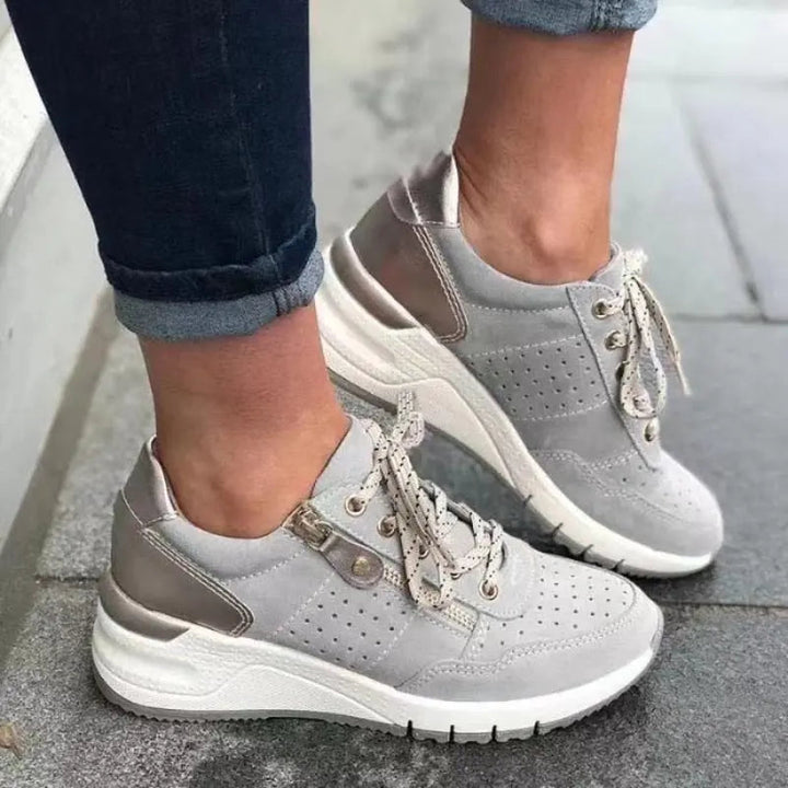 Scarpe da ginnastica grigie da donna con suola bianca, design moderno e lacci, indossate su pavimento grigio. Sneakers casual eleganti e comode.
