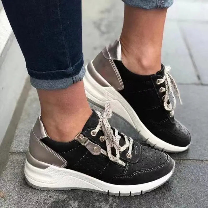 Scarpe da ginnastica nere e argento con lacci bianchi, indossate su pavimento grigio. Sneakers moda donna, comode e trendy.