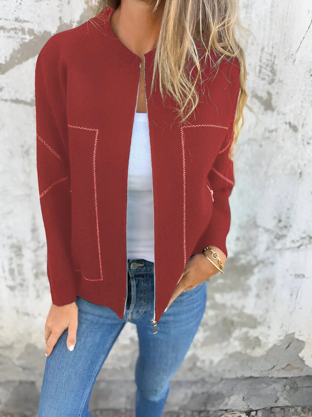 Giacca rossa da donna con zip, indossata su top bianco e jeans blu. Moda casual autunnale, stile elegante e moderno.