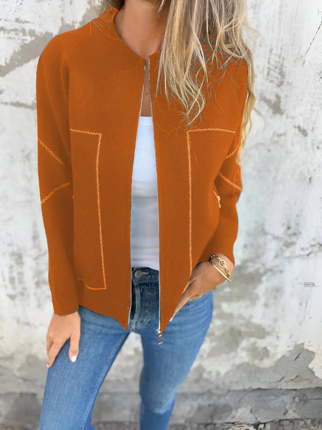 Giacca arancione donna, aperta su top bianco, abbinata a jeans blu. Moda autunnale casual, stile urbano, tessuto morbido.