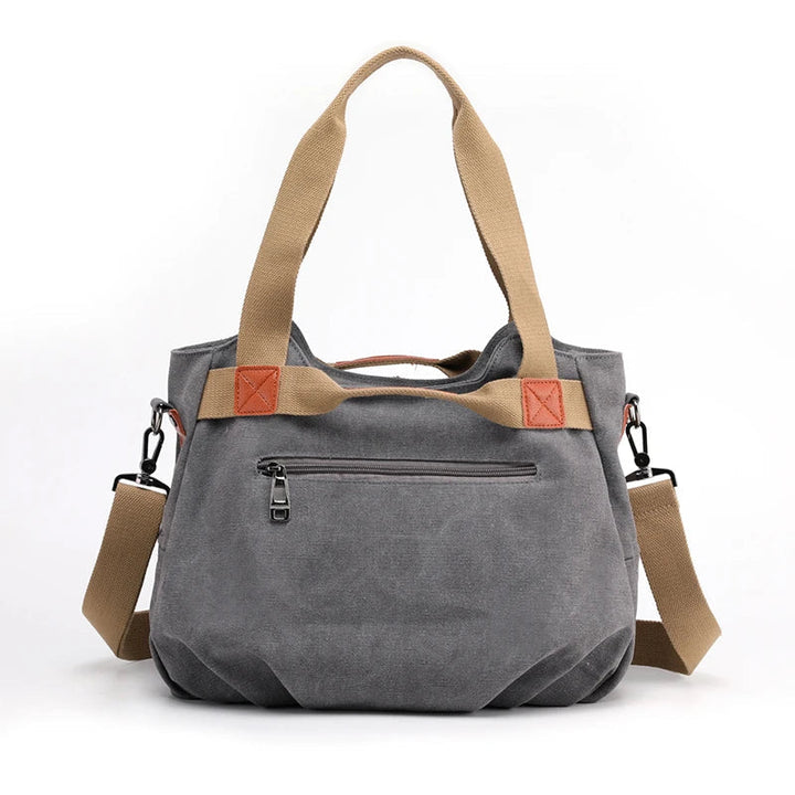 Borsa a tracolla in tela grigia con manici beige, tasca frontale con zip, dettagli in pelle marrone, ideale per moda casual e uso quotidiano.