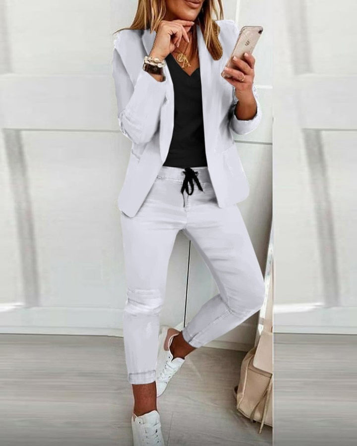 Donna in abbigliamento casual elegante: blazer bianco, t-shirt nera, pantaloni bianchi, sneakers bianche. Outfit moderno e alla moda.