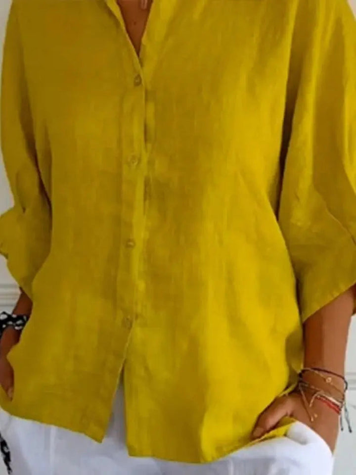 Camicia donna in lino giallo senape, maniche lunghe, abbinata a pantaloni bianchi. Moda estiva casual, abbigliamento leggero e traspirante.