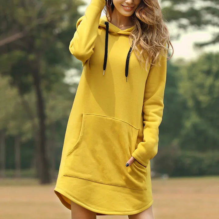 Donna con felpa gialla con cappuccio, tasca frontale e lacci neri, in un parco. Moda casual autunnale, abbigliamento comodo e trendy.