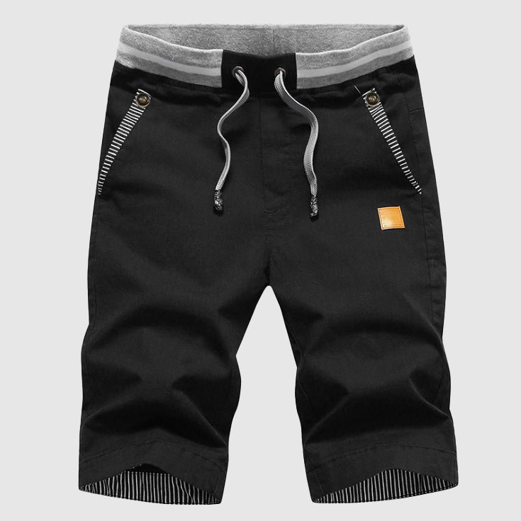 Pantaloncini neri da uomo con coulisse, tasche con zip, dettagli a righe e toppa decorativa. Ideali per moda casual e sportiva.