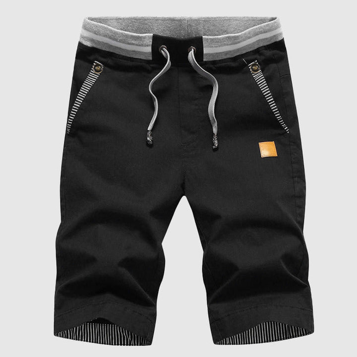 Pantaloncini neri da uomo con coulisse, tasche con zip, dettagli a righe, e bordo grigio. Ideali per sport e tempo libero. Moda casual estiva.