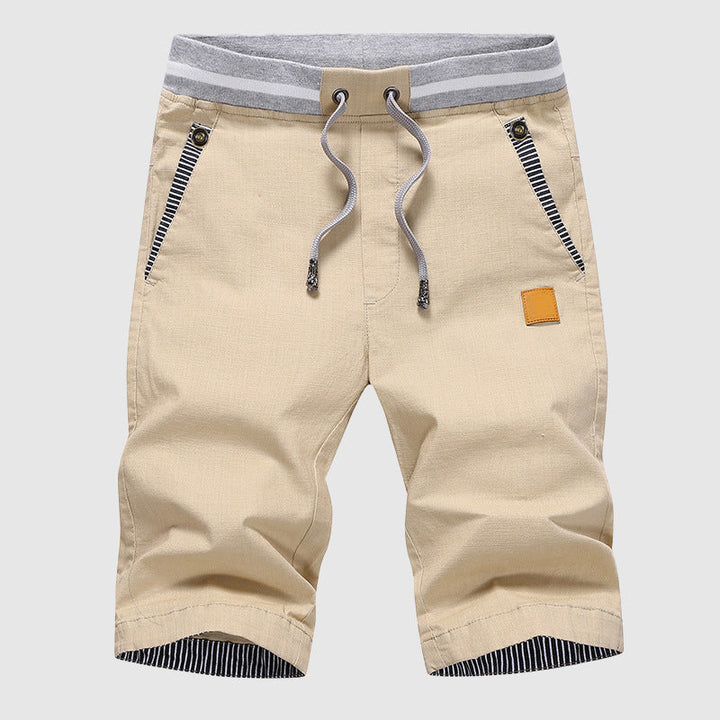 Pantaloncini beige da uomo con coulisse, tasche con zip e dettagli a righe. Design casual, ideale per l'estate. Moda maschile, abbigliamento estivo.