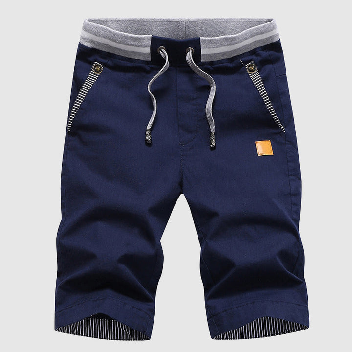 Pantaloncini uomo blu scuro con coulisse, tasche con zip, dettagli a righe, cintura elastica grigia. Ideali per moda casual estiva.