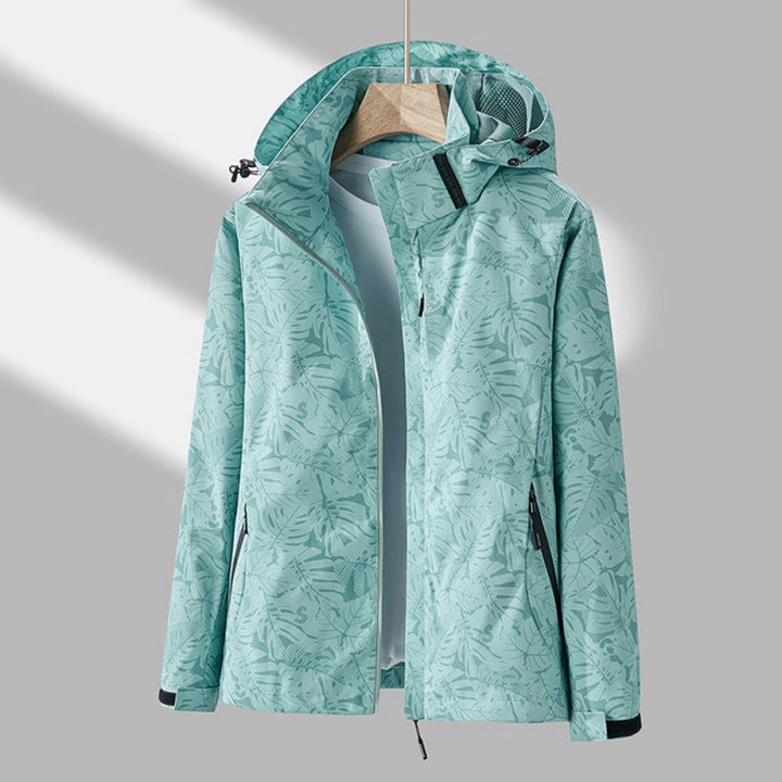 Giacca impermeabile donna verde menta con cappuccio, motivo foglie, chiusura zip, tasche laterali, ideale per escursioni e attività outdoor.