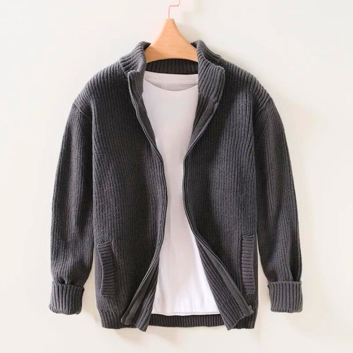 Giacca cardigan in maglia grigia con zip, appesa su gruccia, sopra maglietta bianca. Moda uomo, abbigliamento casual, stile autunnale.