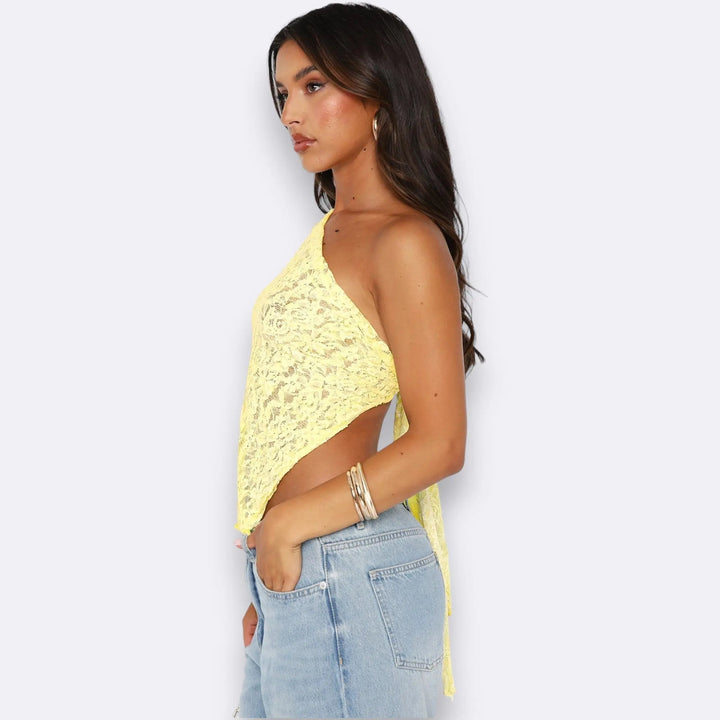 Modella con top monospalla in pizzo giallo, jeans a vita alta, orecchini a cerchio e bracciali. Moda estiva donna, abbigliamento casual chic.