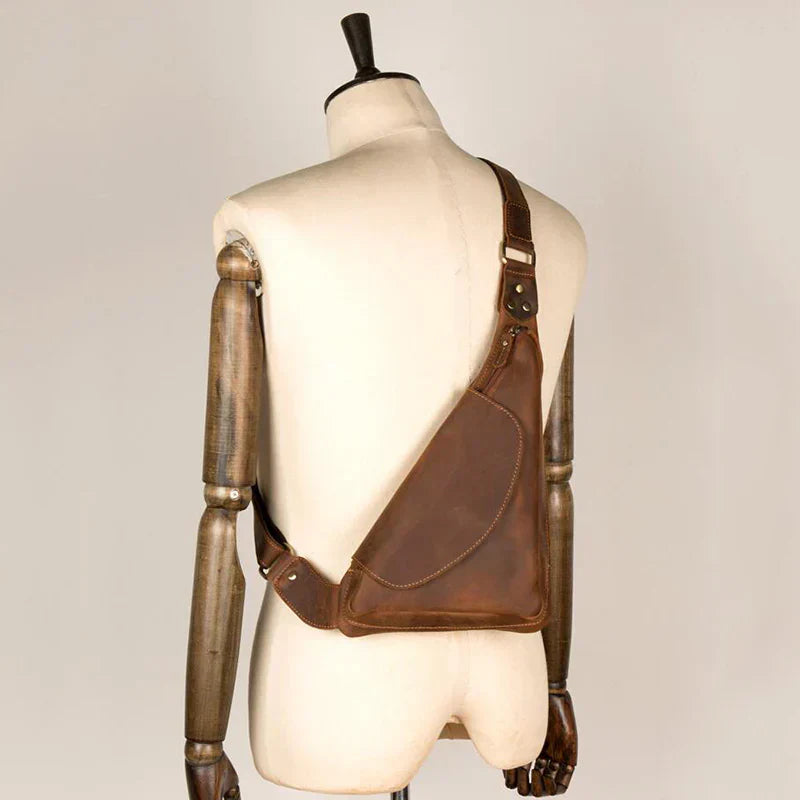 Zaino monospalla in pelle marrone su manichino, design ergonomico, stile vintage, ideale per uomo, accessorio moda, alta qualità artigianale.