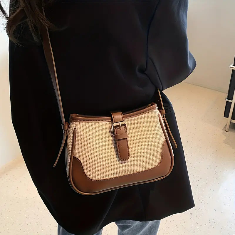 Borsa a tracolla in pelle marrone e tessuto beige, indossata su giacca nera. Design elegante, ideale per moda donna e accessori di tendenza.