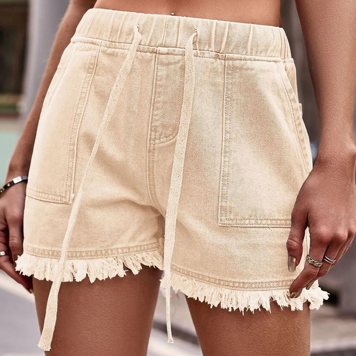 Shorts in denim beige con frange, vita alta, tasche frontali, cordoncino regolabile. Stile casual estivo, moda donna, abbigliamento trendy.