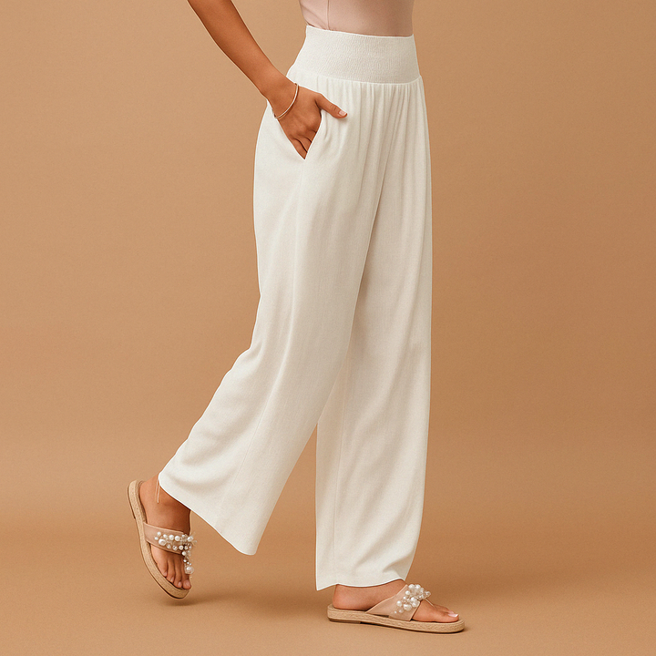 Pantaloni bianchi larghi da donna con tasche, indossati con sandali beige decorati con perle. Moda estiva elegante e comoda.
