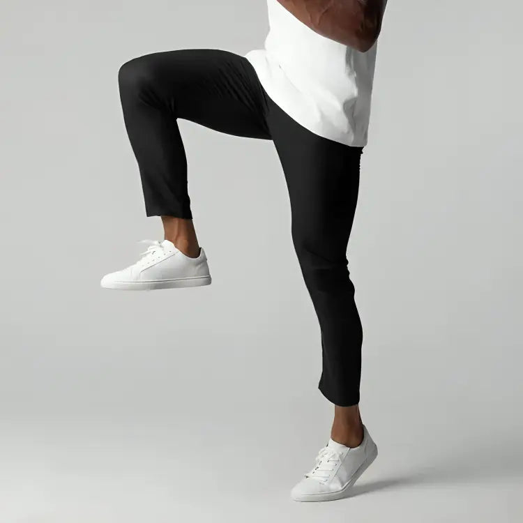 Pantaloni sportivi neri da uomo, elasticizzati, indossati con scarpe da ginnastica bianche e maglietta bianca. Ideali per fitness e allenamento.