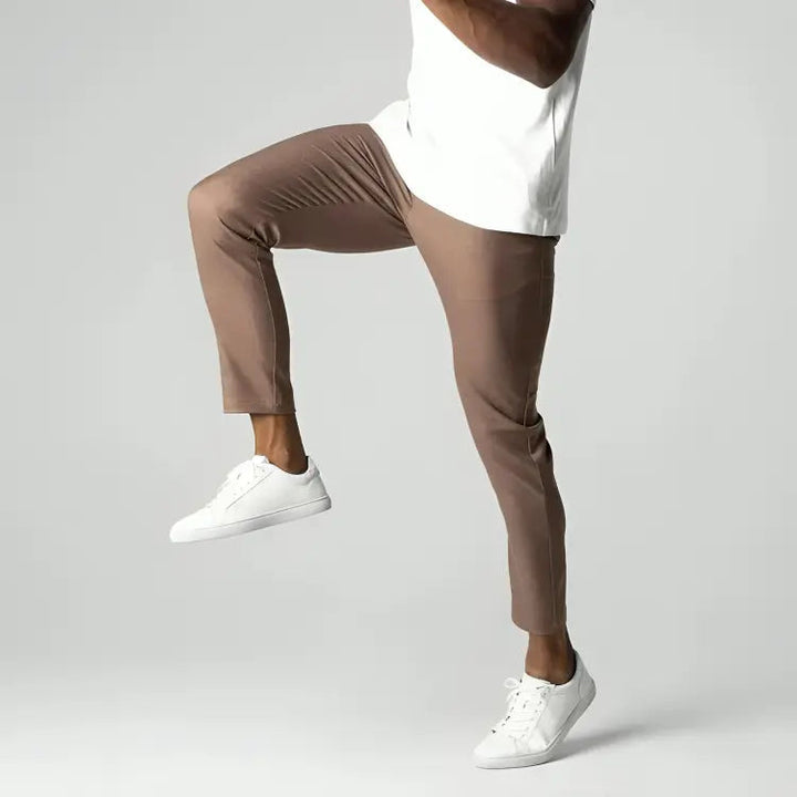 Pantaloni marroni da uomo, vestibilità slim, abbinati a scarpe da ginnastica bianche e maglietta bianca. Stile casual, moda maschile moderna.