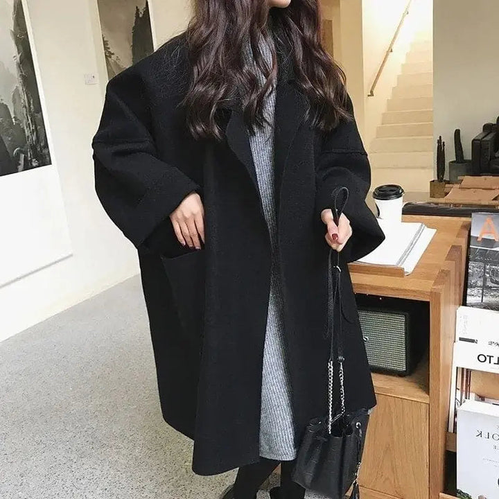 Donna con cappotto nero oversize, abito grigio, borsa a tracolla nera. Moda invernale elegante, abbigliamento casual chic.