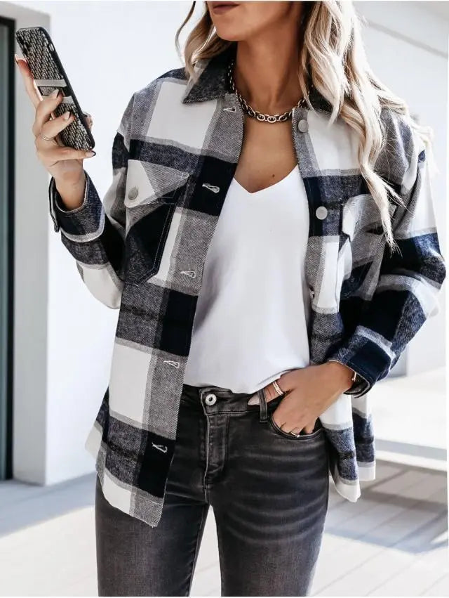 Donna con camicia a quadri bianca e nera, smartphone in mano, jeans grigi. Moda casual autunnale, stile urbano, tendenze abbigliamento femminile.