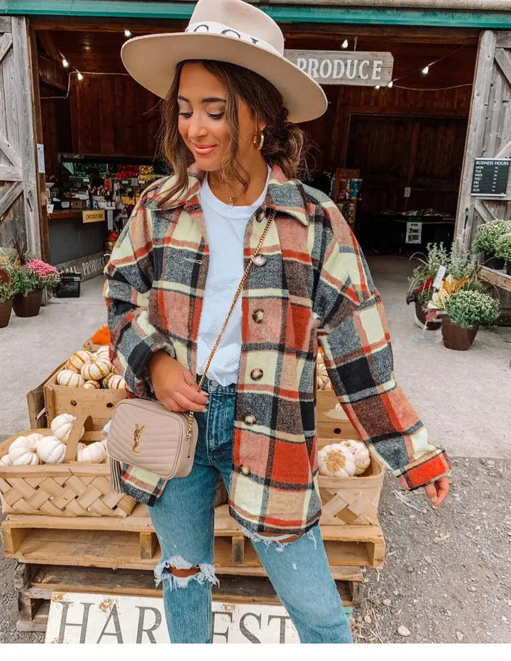 Donna con cappotto a quadri autunnale, jeans strappati e cappello beige davanti a mercato agricolo. Moda autunnale, stile casual, shopping locale.