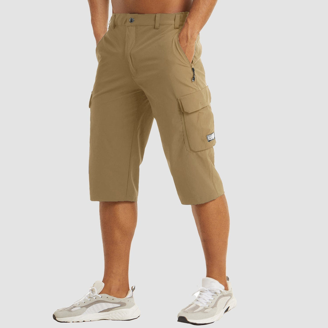 Pantaloncini cargo beige da uomo, lunghezza al ginocchio, con tasche multiple e chiusura a zip, indossati con scarpe sportive bianche.