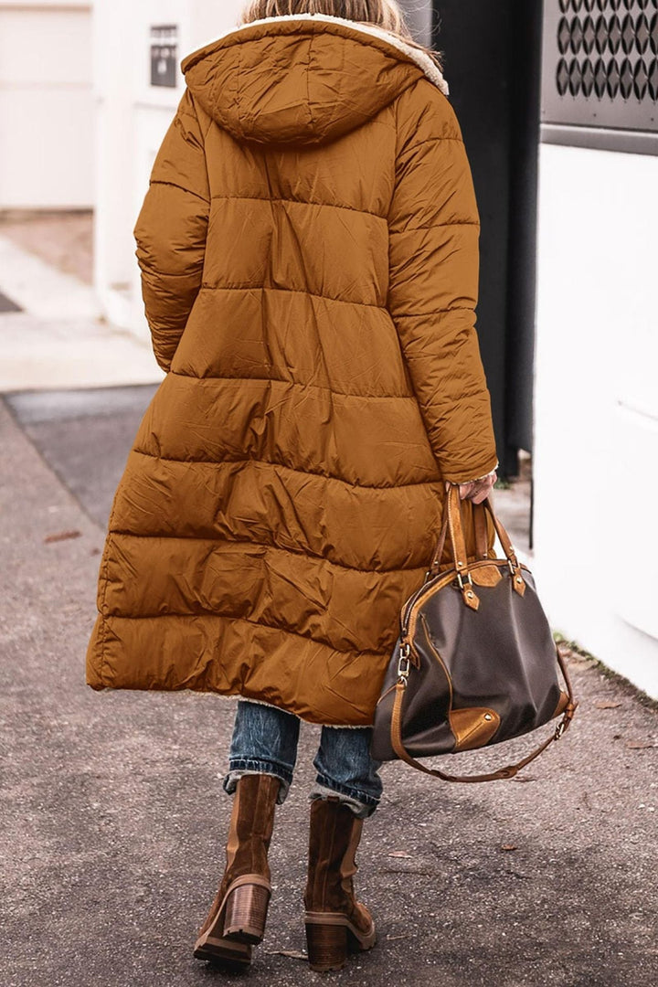 Donna con cappotto lungo marrone trapuntato, cappuccio, stivali invernali e borsa in pelle marrone. Moda invernale, abbigliamento caldo, stile urbano.