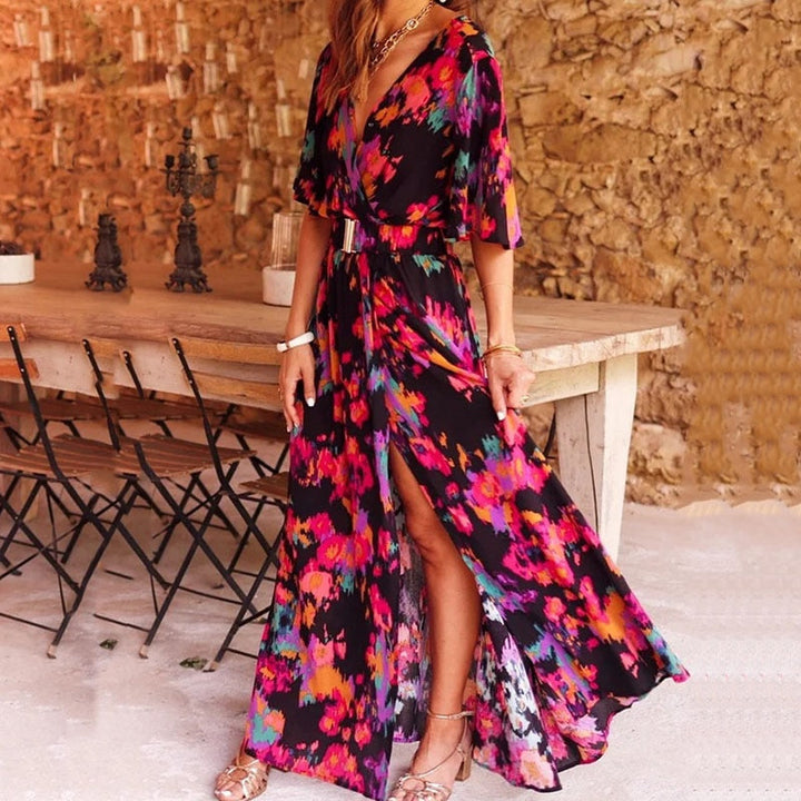 Abito lungo floreale colorato, donna, con spacco, maniche corte, sfondo rustico, tavolo in legno, sedie pieghevoli, moda estiva elegante.