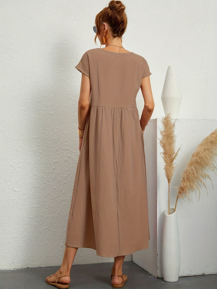 Abito lungo marrone chiaro, donna di spalle, sandali beige, vaso bianco con pampas, moda estiva casual, abbigliamento femminile elegante.