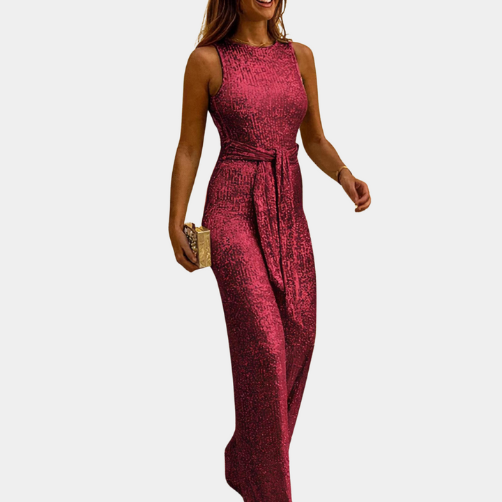 Donna in elegante tuta lunga rossa con paillettes, senza maniche, cintura in vita, clutch dorata. Abbigliamento da sera glamour.
