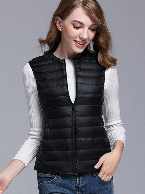 Donna con gilet nero imbottito, maglia bianca a maniche lunghe e jeans. Moda autunnale, abbigliamento casual elegante.