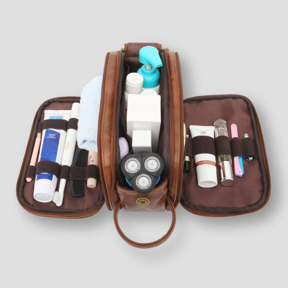 Borsa da toilette in pelle marrone aperta, contenente articoli da toeletta come rasoio elettrico, spazzolino, deodorante e prodotti per la cura personale.
