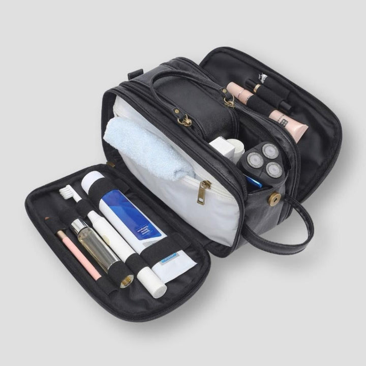 Borsa da toilette nera aperta con scomparti multipli, contenente articoli da viaggio come spazzolino, tubetti di crema e asciugamano.