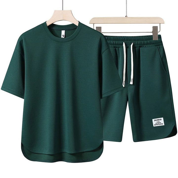 Set coordinato uomo verde scuro, maglietta a maniche corte e pantaloncini con coulisse. Abbigliamento casual estivo, tessuto leggero e traspirante.