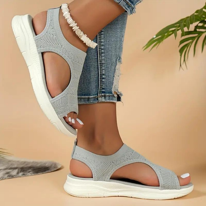 Sandali estivi grigi da donna con suola bianca, design traforato, indossati con jeans strappati. Scarpe comode e alla moda per la stagione calda.